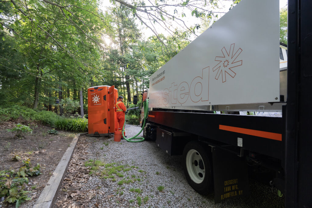 A Wasted employee cleaning a unit placed on the street with trees in the background